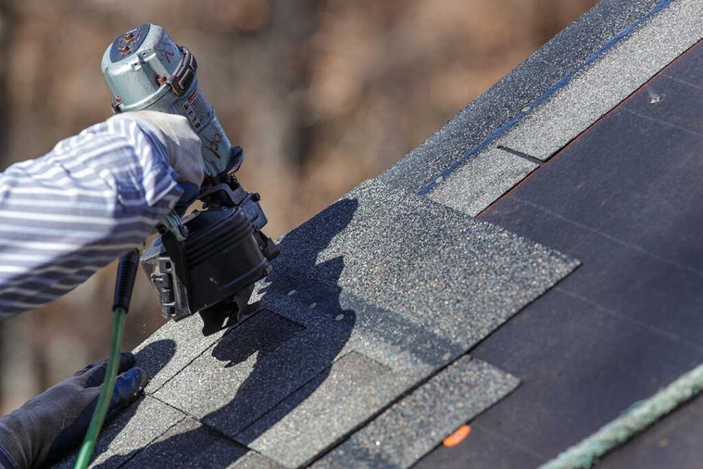 A homeowner examining damaged shingles on a house roof after a recent storm.