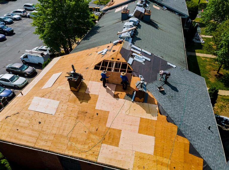 A close-up view of a person holding roof warranty papers next to shingles on a home roof.